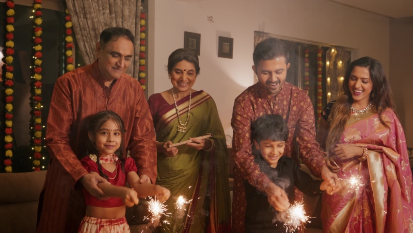 Ethnic Indian Hindu happy smiling cute young boy and a girl or kids in traditional attire playing with firecrackers or sparklers with the help of family elders or parents during Diwali festival. Royalty-Free Stock Footage #1095190943