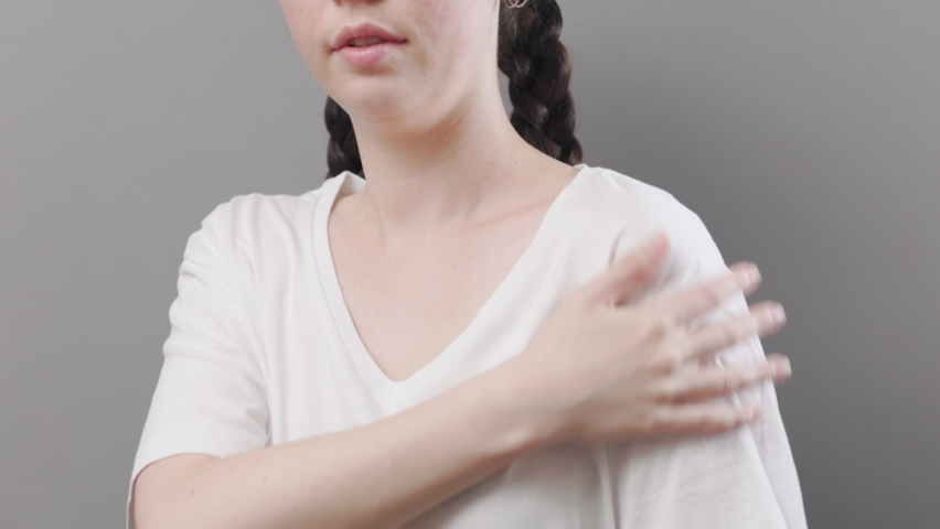 Arthritis and chondrosis. A young woman massages shoulder with her hand, feeling pain. Studio background. The concept of health insurance and injuries of ligaments and joints.