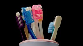 Close-up of toothbrushes in a glass rotate on a black background. Caring for teeth, multicolored toothbrushes. Toothbrushes on a turntable