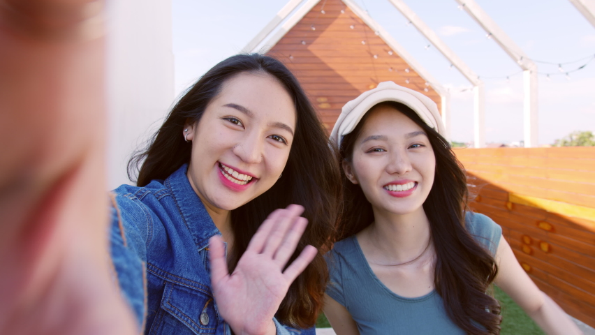 POV of young asian woman in fashion clothes with friend talking via video call to smartphone camera outdoor