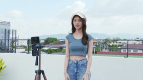 Young Asian woman created her dancing video by smartphone camera on rooftop outdoor at sunset. To share video on social media application