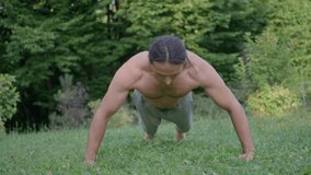 Athlete with long black hair, performs push-ups, trains in the summer on grass, slow motion 