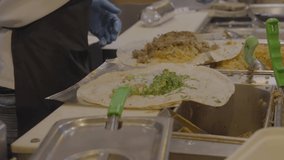This video shows the hands of a restaurant cook assembling burritos.