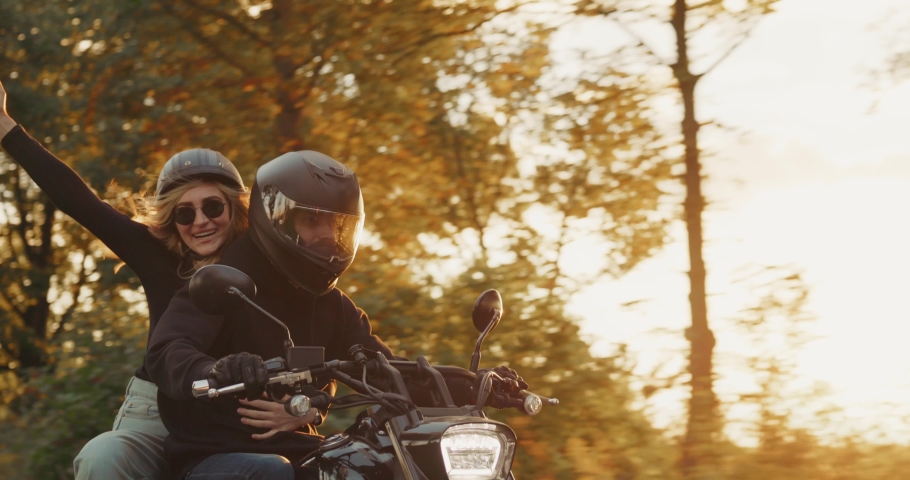 Man motorcyclist with girlfriend riding on motorbike on the road at sunset during fall. Man drive his motorcycle racing on empty highway on a sunny day