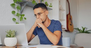 a young man using a laptop at home and looking thoughtful 