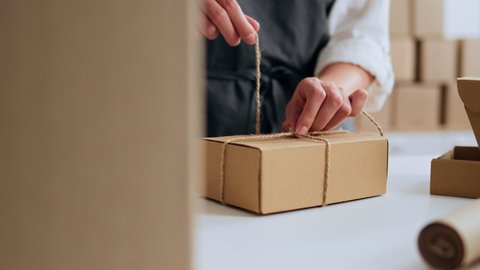 Small business owners packing cardboard boxes for customers who make online orders through the Internet, e-commerce, packaging cardboard boxes tying jute string rope
 Arkivvideo