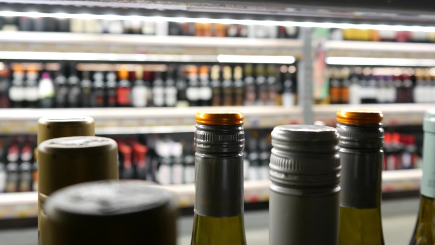 Close-up of many beautiful bottles of white wine and a male buyer takes one