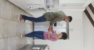 Vertical video of happy african american couple dancing in kitchen. Spending quality time at home together concept.
