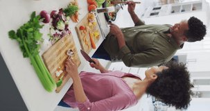 Vertical video of happy african american couple cooking in kitchen. Spending quality time at home together concept.