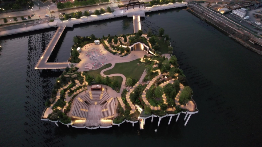 An aerial view of Little Island in Manhattan early in the morning. The camera, tilted down dolly out and boom up high over the Hudson River from the closed, illuminated park and the westside highway.