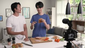 Young Asian Gay couple blogger influencer vlogger shooting video in kitchen. LGBT couple live- streaming cooking class from home.
