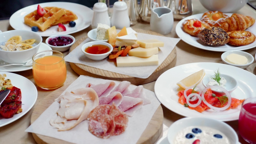 Brunch or lunch in luxury restaurant. Table full of delicious food - cheese, salmon, ham, bakery and juices. Buffet food in hotel. Morning food with various snacks and appetizers. Royalty-Free Stock Footage #1095229369