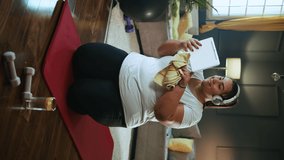 Vertical shot of overweight young woman using tablet to video chat with trainer after online workout at home