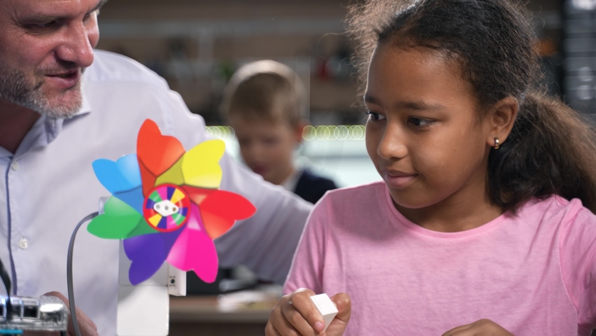 STEM education. Elementary school african girl learning robotics wind engine mill with her male teacher in class. Smart kid learning electric toy at robotics engineering laboratory. 4K footage