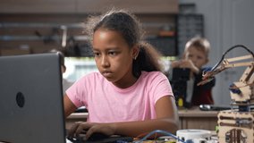 Portrait of smart african school girl programming software for robotics engineering class using laptop, looking at camera and smiling with school class on background. STEM education concept 4K - Powered by Shutterstock - Get 15% off with code: PIKWIZARD15