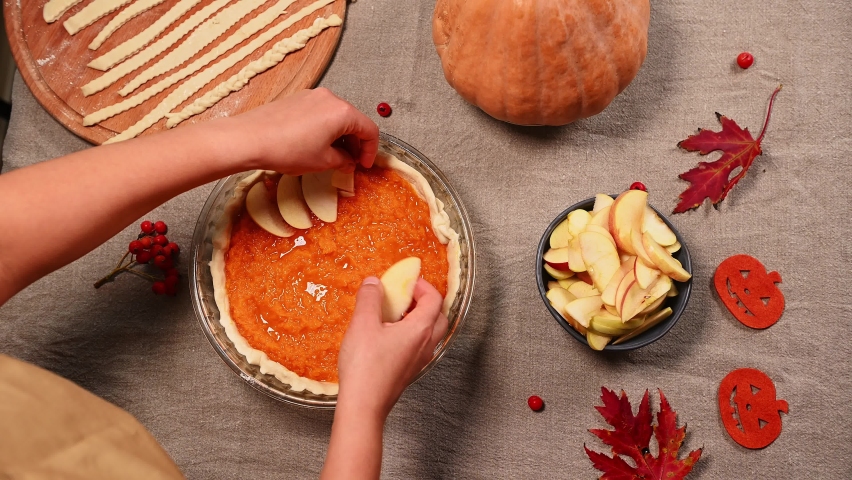 View from above on the hands of a housewife, spreading apple slices in a circle on top of pumpkin puree in rolled out dough in the baking dish, while preparing a tasty pumpkin pie for Thanksgiving Day | Shutterstock HD Video #1095234525