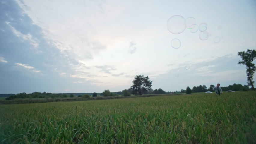 Slow motion video of children running after soap bubbles and popping them. Happy family on a walk in the park. Cheerful smiling children. Time spent together. High quality 4k footage