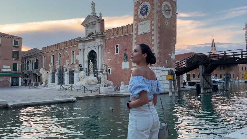 one person, a woman 30 years old. woman tourist visiting the Arsenal landmark in venice italy. She is romantically dressed in a blue top and denim shorts. Royalty-Free Stock Footage #1095238193