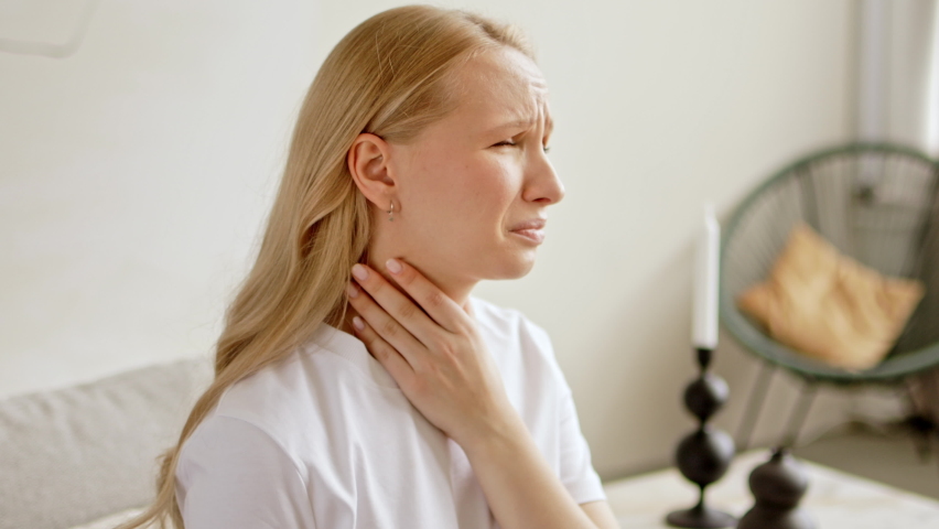 Woman touches her sore throat has difficulty swallowing. Painful neck and frowning, thyroid disorders. Angina or tonsils inflammation. Royalty-Free Stock Footage #1095239257