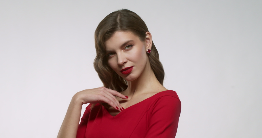 Cheerful young woman with red lips posing as female model with beautiful makeup on her face, wearing elegant dress, isolated on white studio background