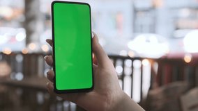 Woman using Chroma Key Smartphone while Sitting, Looking at the Green Screen. Female Using Mobile Phone. Over the Shoulder Closeup Tracking Shot Focus on Display