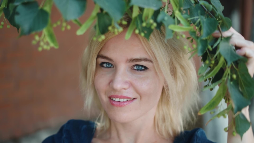 Portrait of a beautiful young blonde in a city park. She smiles and enjoys the good weather. Slow motion.