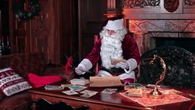 Busy Santa looking through the Christmas cards. Preparation for holidays. Santa Claus working in his cabin near fireplace. - Powered by Shutterstock - Get 15% off with code: PIKWIZARD15