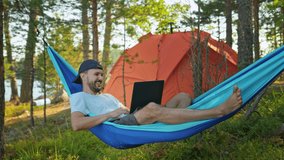 Happy man camper talking calling on video on laptop laying in hammock in camp. Go Everywhere