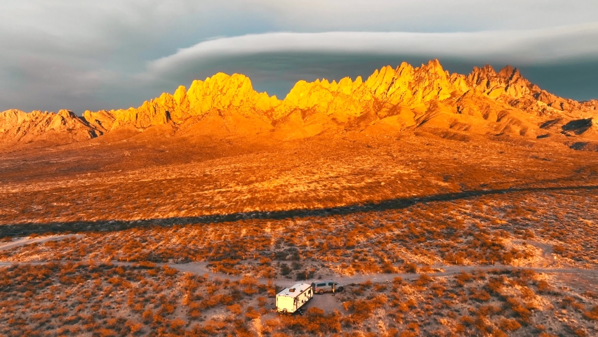 The Organ Mountains Rugged Peaks Tower Over The Chihuahuan Desert In Southern New Mexico, Camper Van Parked At Sunset - aerial pullback