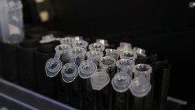 Vials with samples are getting put inside of an analyzing machine. Scientist holds a chemical sample bottle. doctor works in a laboratory, Bio samples being loaded into analyzing machine. 4 k video