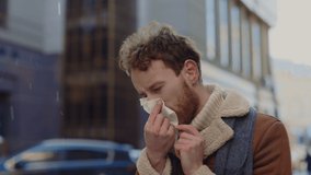 Caucasian man with beard in scarf blowing his nose into handkerchief while standing outdoors. Man feeling sick blowing nose using handkerchief. People and health problems concept - Powered by Shutterstock - Get 15% off with code: PIKWIZARD15