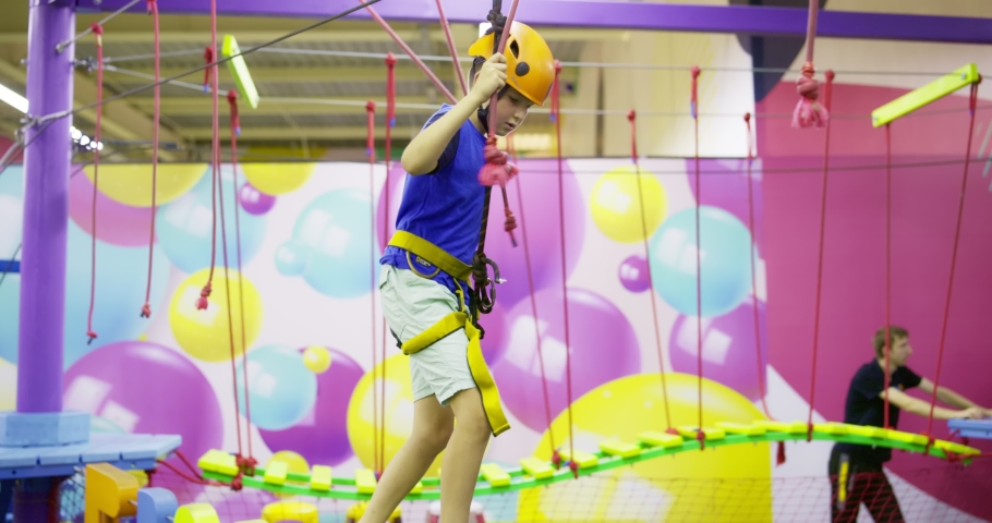 Boy in protective gear holding safety rope and passing obstacle course