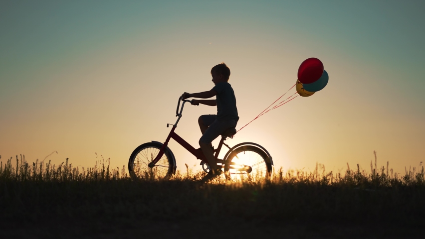 Dream child. Silhouette of child on bicycle plays in park. boy rides through natural green park with balloons. Play with balloons on bike. boy dreams of learning to ride bicycle in nature. Royalty-Free Stock Footage #1095282053