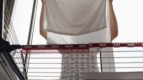Woman hanging wet clean cloth on laundry drying rack in balkony at home. Close up of female hands hanging washed clothes, towels, linens on clothes wire dryer