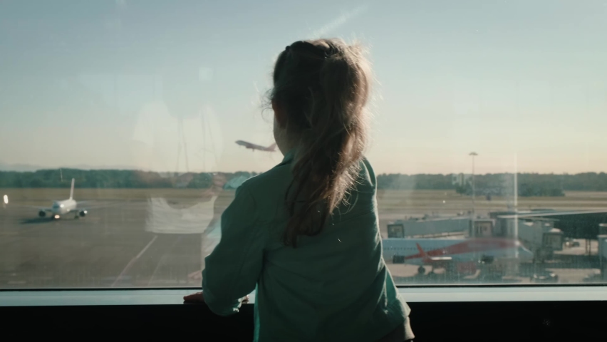 View from the back of a little baby girl waving through an airport terminal window to a taking off jet. Daughter saying goodbye to the departing plane. High quality 4k footage Royalty-Free Stock Footage #1095284055