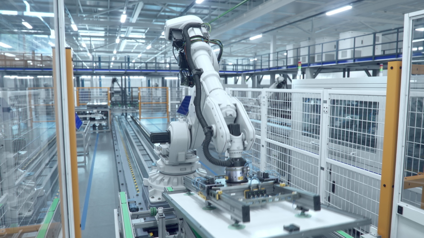 White Industrial Robot Arm at Production Line at Modern Bright Factory. Solar Panels are being Assembled on Conveyor. Automated Manufacturing Facility