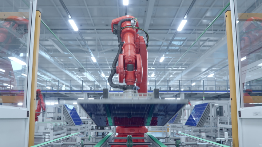 Orange Industrial Robot Arm Moving Solar Panels at Production Line at Modern Bright Factory. Solar Panels are being Assembled on Conveyor. Automated Manufacturing Facility. POV view from the Line