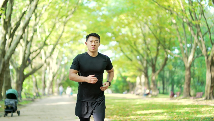 sporty young asian runner running on alley in city urban park. Morning jogging of an athletic man outdoors in nature. Sport Male athlete jogger in black sportswear, slow motion Royalty-Free Stock Footage #1095296977