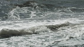Sea waves glisten in the sun and bubbling foam in slow motion video. A long shot taken with a tripod