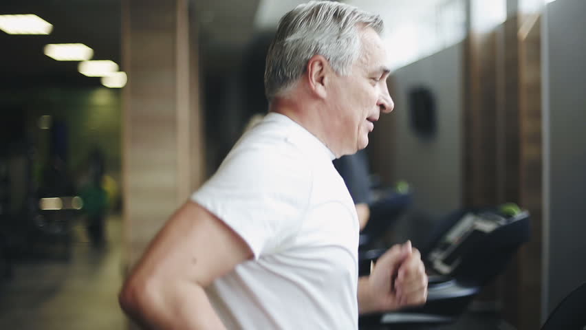 Senior man exercising on a treadmill in the gym. Right profile face footage