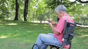 Asian elderly man in a wheelchair in the garden play mobile online social media Enjoy life on vacation. Retirement health care concept. life insurance health insurance