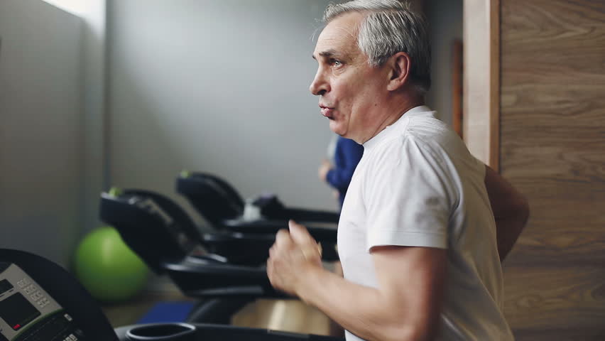 Senior man exercising on a treadmill in the gym. Left profile face footage
