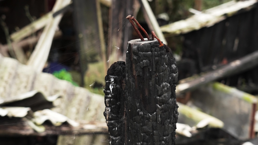 Black burnt log with rusty bent nails of a house burned by fire. Wood coal and ash texture