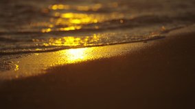Slow-motion video of ocean waves splashing on sand. Golden sun reflecting on water and sand