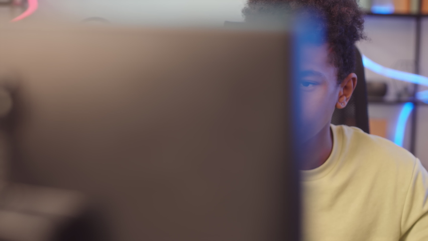 Biracial teenage pc gamer sitting at desk in front of computer monitor and playing video game Royalty-Free Stock Footage #1095315311