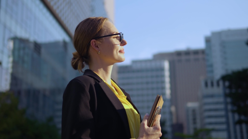 Grateful Happy Inspired Businesswoman in Glasses Looking far Away at Sunset Sky Standing Outside Against Modern Financial District Buildings - orbit shot Royalty-Free Stock Footage #1095317401