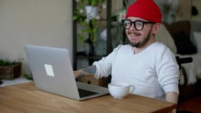 Young man with disability wearing red cap talking in video conference
