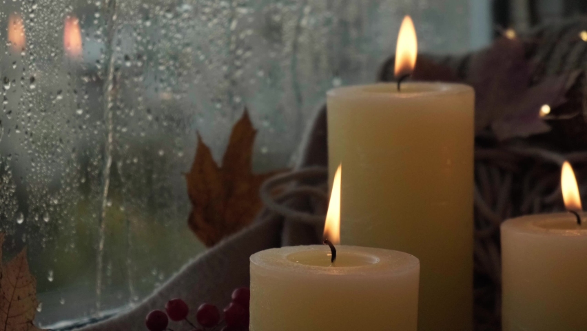 Thanksgiving and Hello Fall, celebrating autumn holidays at cozy home on the windowsill Hygge atmosphere Autumn leaves, spices and candle on cozy knitted sweater in warm yellow lights. Raining Outside | Shutterstock HD Video #1095324361