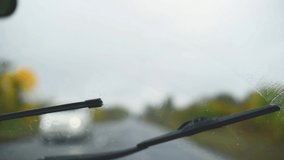 View from the interior of the car on windshield in rainy autumn weather.Wipers wash away raindrops and long road on background horizontal video. Travelling by car	
