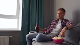A young man drinking beer while sitting on the couch. Concept of free time, sport and entertainment. 